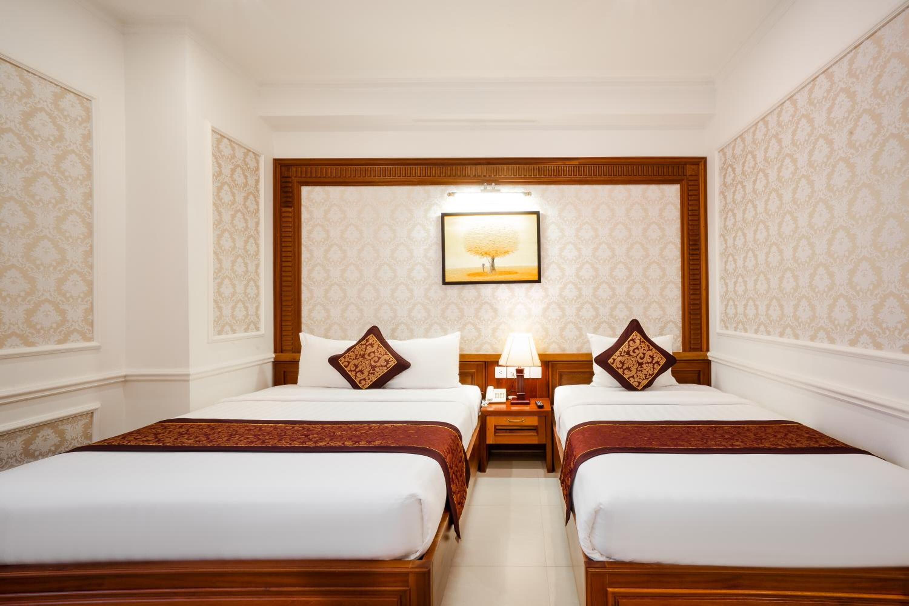 A hotel room with two beds, a nightstand with a lamp, and a framed picture on the wall.