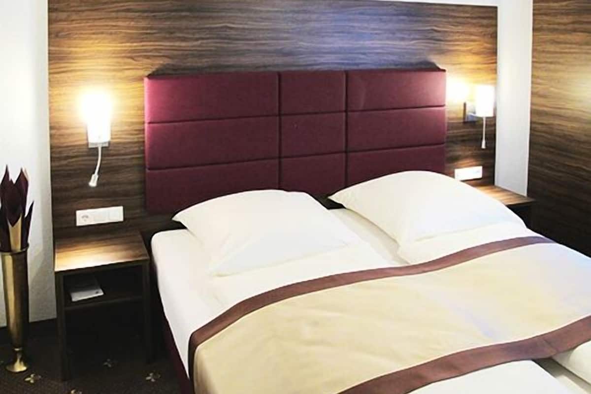 Camera d'albergo con un letto grande, una testiera in legno, lampade sui comodini e un comodino.