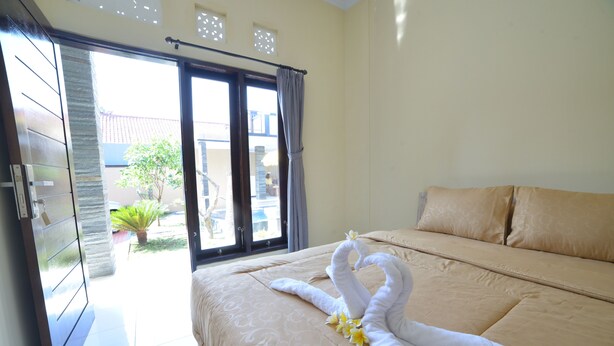 A hotel room with a bed, a sliding glass door leading to a balcony, and a view of the outside. - Ratu Guest House (Kedonganan)