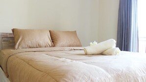 A neatly made bed with beige bedding and pillows, a rolled towel, and a flower on the bed. - Ratu Guest House (Kedonganan)