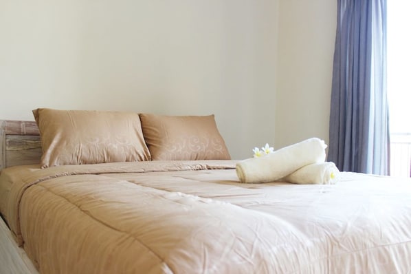 Una cama bien hecha con ropa de cama color beige y almohadas, una toalla enrollada y una flor sobre la cama.