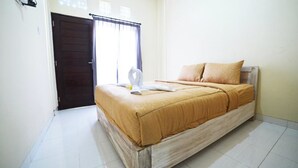 A hotel room with a bed, a door, and a window with curtains. - Ratu Guest House (Kedonganan)