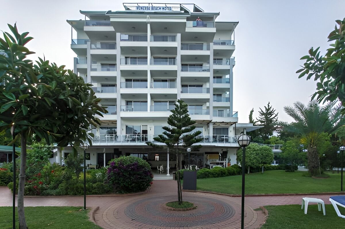 A multi-story hotel with a central courtyard, surrounded by greenery and a paved walkway.