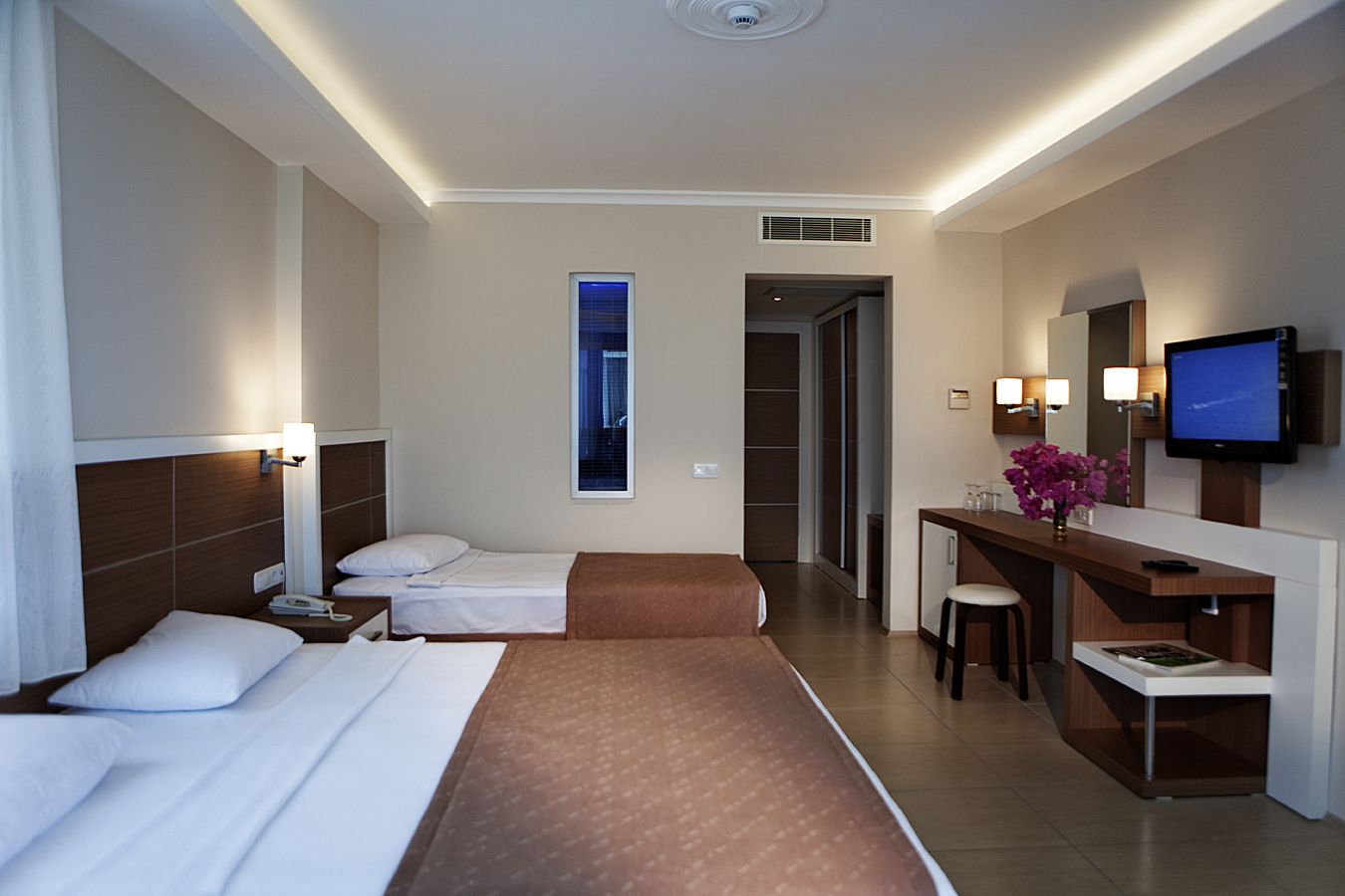 A hotel room with two beds, a desk with a chair, a TV, and a window with a view.