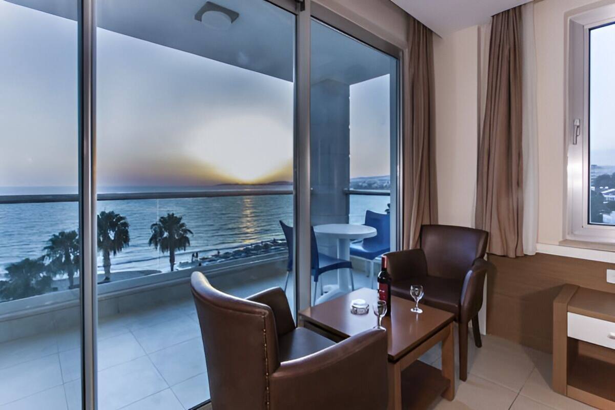 Un balcón con vistas al mar y palmeras, una mesa con una copa de vino y una silla.