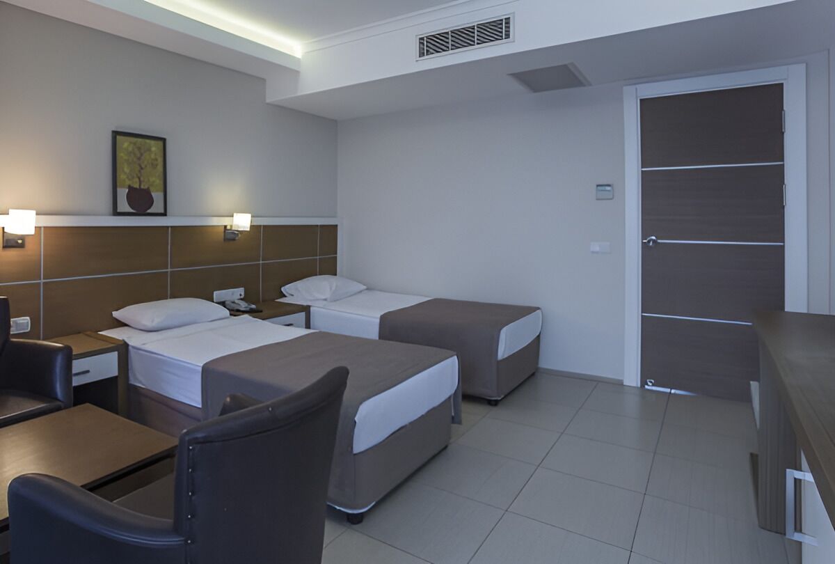 Habitación de hotel con dos camas, un escritorio, una silla, una mesita y una puerta.