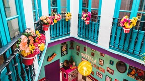 A brightly colored building with teal and white walls, multiple balconies with flower baskets, and a vibrant interior with various decorations. - Rio Hostel (Seville)