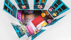 A top-down view of a room with teal-framed windows, a red carpet, and various pieces of furniture. - Rio Hostel (Seville)