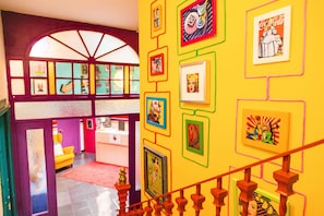 A brightly colored interior with a staircase, framed artwork on the walls, and a yellow carpet. - Rio Hostel (Seville)