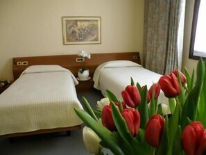 A hotel room with two beds, a nightstand with a lamp, a painting on the wall, and a window with curtains. - Hotel Ristorante Villa Monica (Prata di Pordenone)