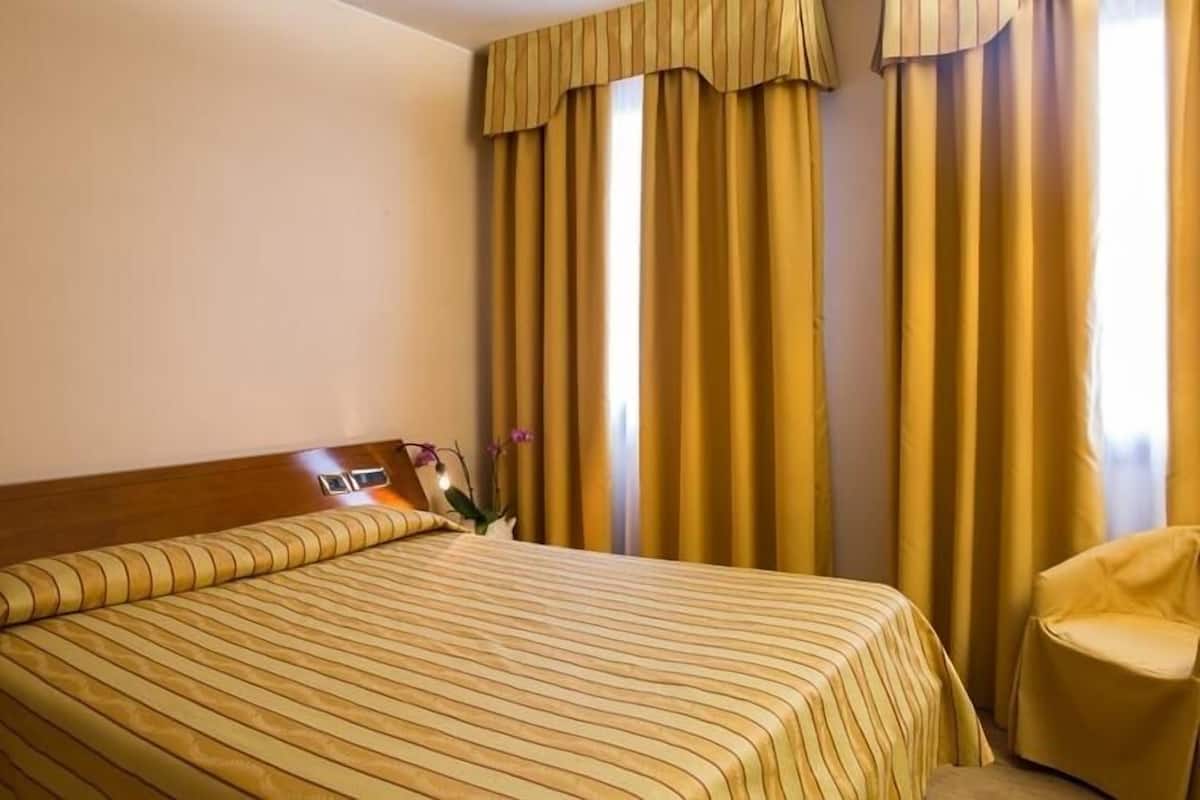 A hotel room with a large bed, a wooden headboard, a chair, and curtains.