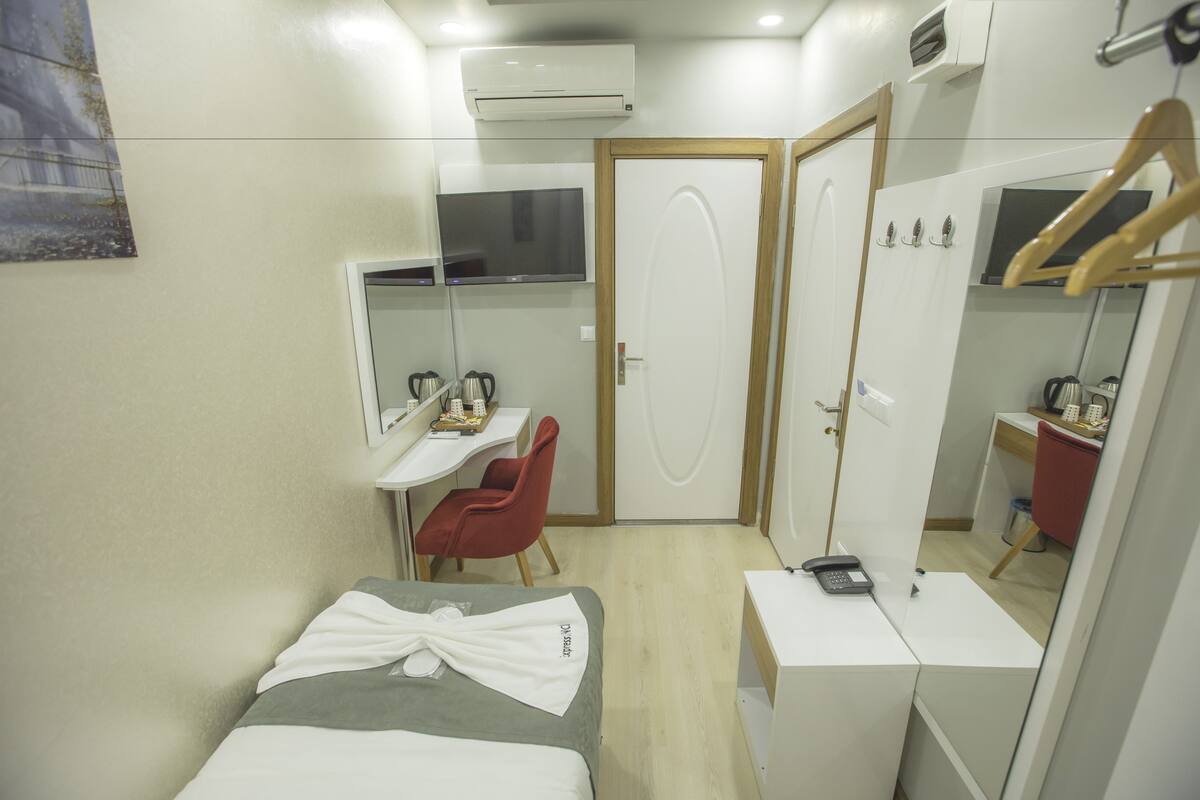 A compact hotel room with a bed, a desk, a chair, a wardrobe, and a mirror.