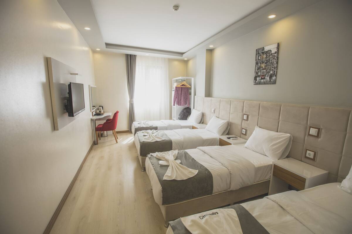 A hotel room with three beds, a TV, a desk, and a chair.