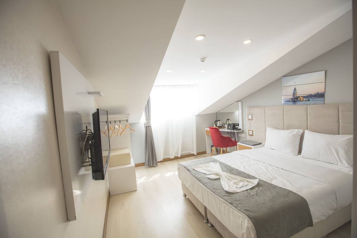 A modern hotel room with a large bed, a desk, and a chair.