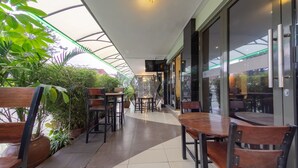 A modern indoor patio area with wooden tables and chairs, surrounded by potted plants. - Hotel Rio (Nairobi)