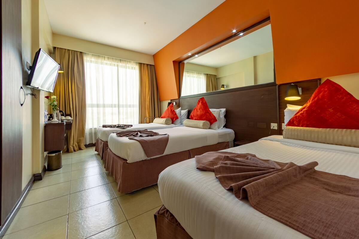 A hotel room with two beds, a TV, a mirror, and a window with curtains.