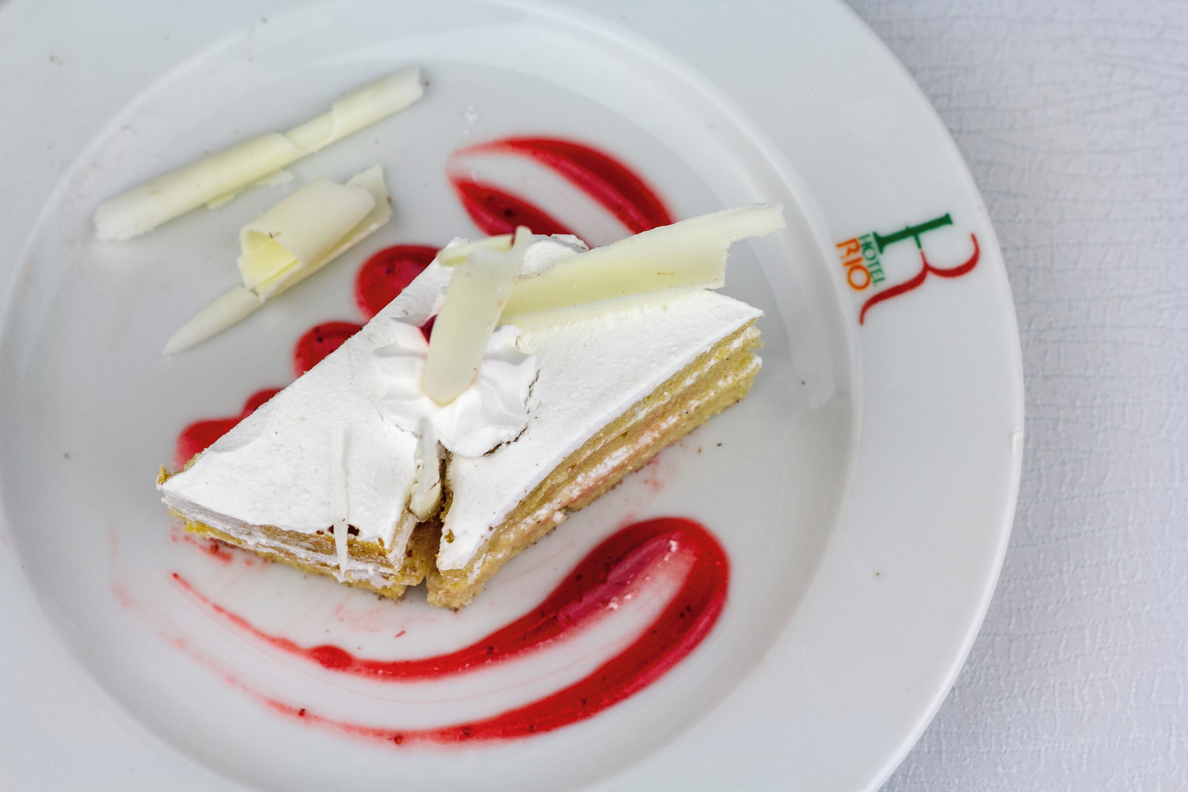 A dessert plate with a slice of cake, whipped cream, and a red sauce.