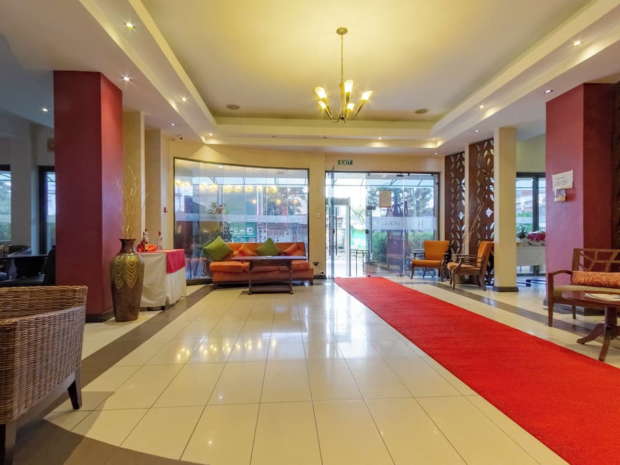 Un hall de hotel con alfombra roja, un sofá, sillas de mimbre y una araña.