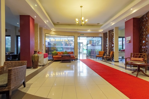 A hotel lobby with a red carpet, a sofa, wicker chairs, and a chandelier.