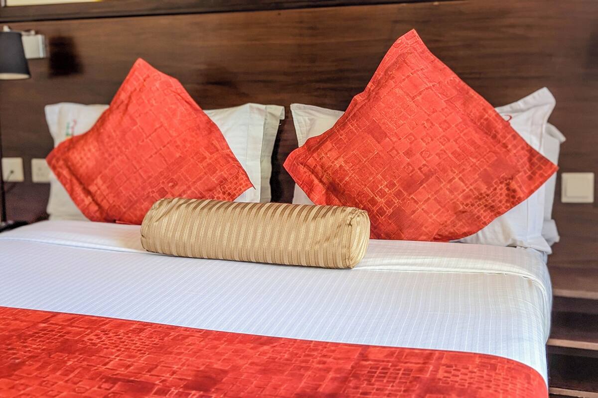 A neatly made bed with a white and red bedspread, two red pillows, and a beige throw pillow.