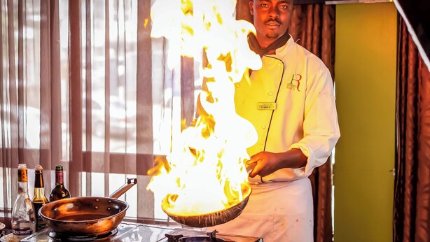A chef performing a flambé with a pan on a stove. - Hotel Rio (Nairobi)