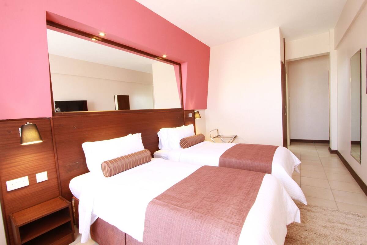 A hotel room with two beds, a large mirror, bedside lamps, a wooden nightstand, and a small table.