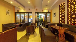 A well-lit indoor seating area with multiple sofas and chairs, a wooden table, and glass doors leading outside. - Hotel Rio (Nairobi)