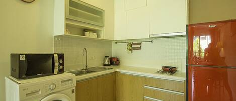 Cocina compacta con lavadora, microondas, fregadero y un refrigerador rojo.