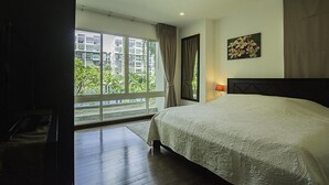 Ein Schlafzimmer mit einem großen Bett, einem Fenster mit Vorhängen und Blick auf Grünfläche.