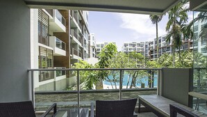 Ein Balkon mit Korbmöbeln, einem Glastisch und Blick auf ein Schwimmbad und Gebäude.