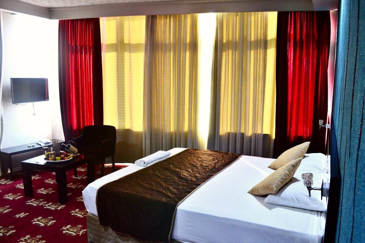 Habitación de hotel con cama, escritorio con silla, televisor y ventana con cortinas.