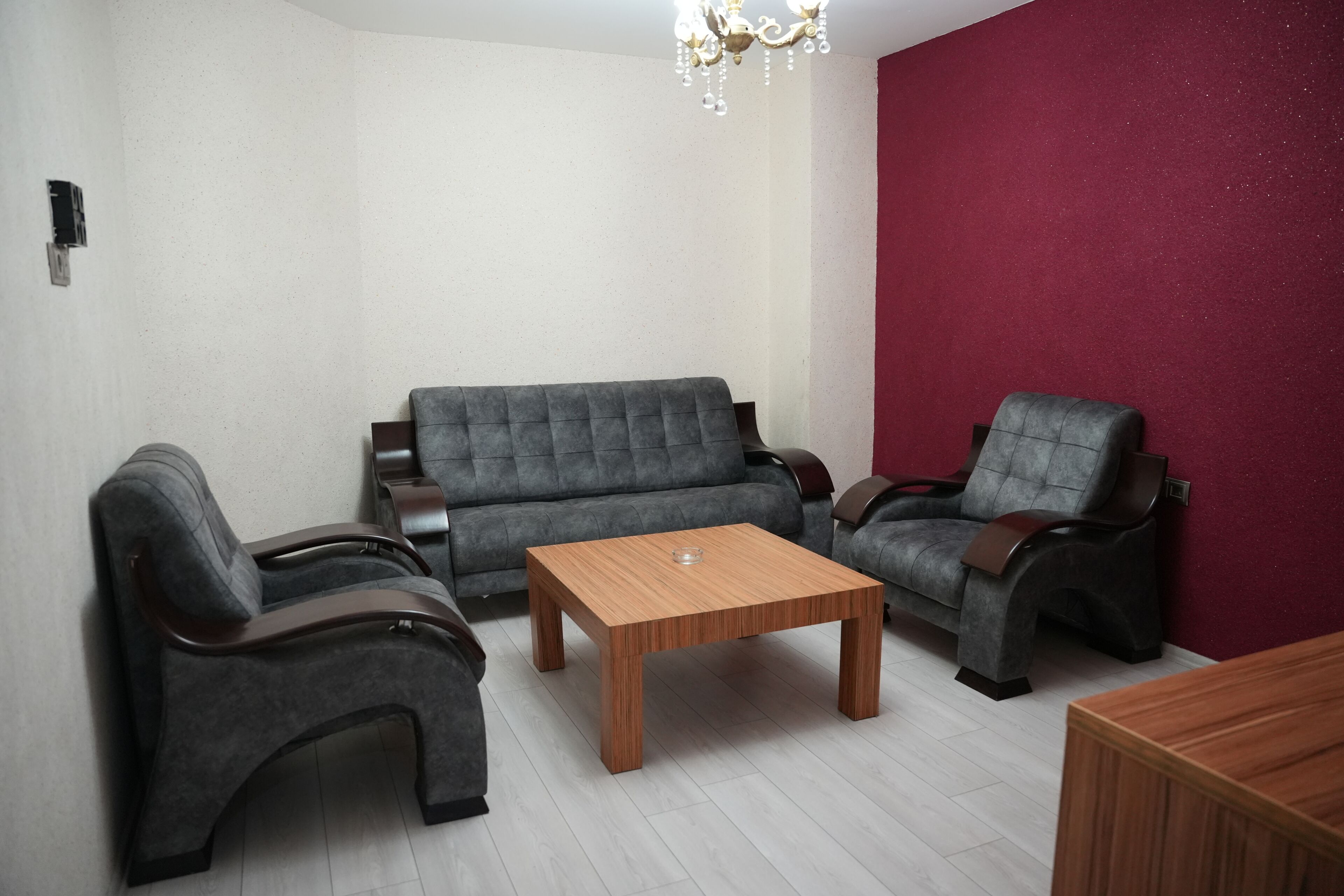 A living room with a grey sofa, two armchairs, a wooden coffee table, and a red accent wall.