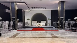 Un vestíbulo amplio con suelo de mármol, un escenario central con alfombra roja y una zona de estar con sofás blancos y sillas traslúcidas.
