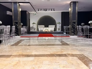 Un vestíbulo amplio con suelo de mármol, un escenario central con alfombra roja y una zona de estar con sofás blancos y sillas traslúcidas.