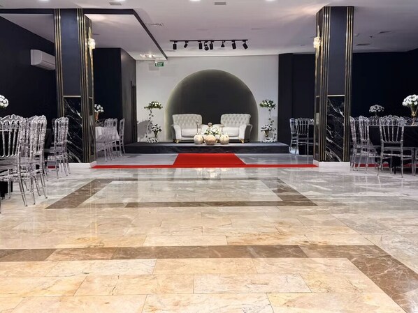 A spacious lobby with a marble floor, a central stage with a red carpet, and a seating area with white sofas and clear chairs.