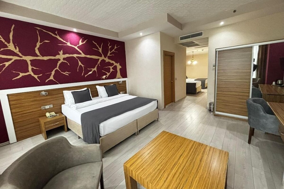A modern hotel room with a large bed, a wooden headboard, a desk, and a chair.