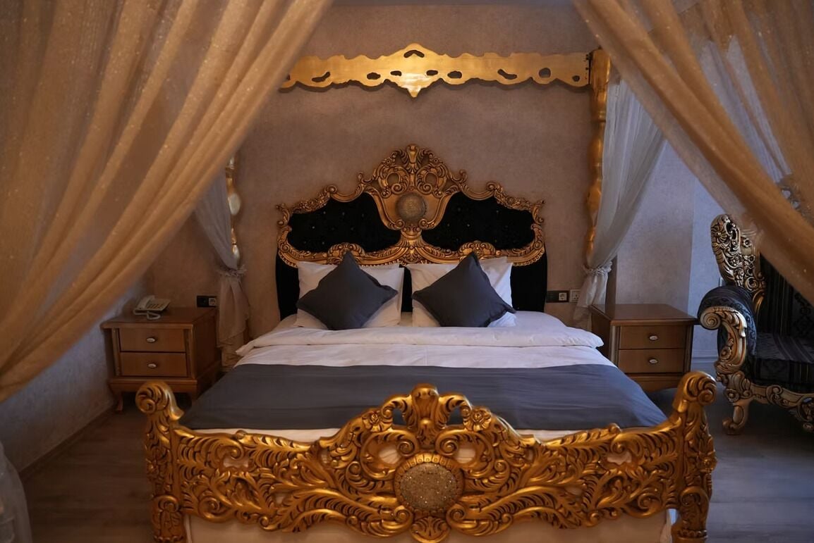 A luxurious bed with an ornate headboard, a canopy, and a nightstand with a telephone.