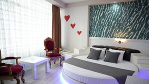 Un dormitorio moderno con una cama, un sillón rojo, una mesa blanca y una pared decorada con corazones.