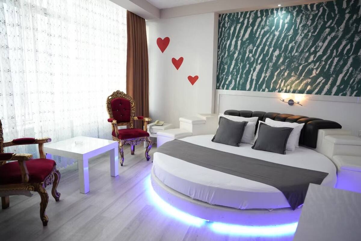 Un dormitorio moderno con una cama, un sillón rojo, una mesa blanca y una pared decorada con corazones.
