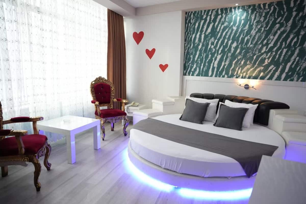 A modern bedroom with a bed, a red armchair, a white table, and a wall with heart decorations.