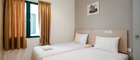 Habitación de hotel con dos camas, paredes color beige, una ventana con cortinas y una obra de arte pequeña en la pared.