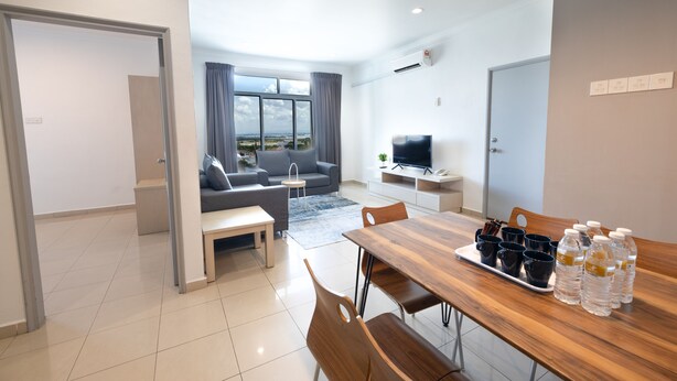 A modern living room with a sofa, a coffee table, and a dining table with chairs. There are bottles of water and cups on the table. - Golden View Serviced Apartment (George Town)