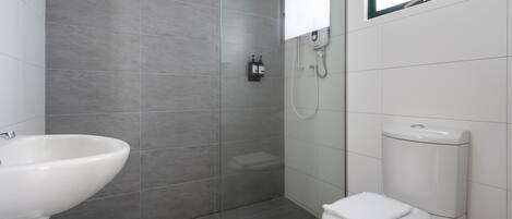 Et moderne badeværelse med en glasafskærmet brusekabine, en hvid vask og et toilet.