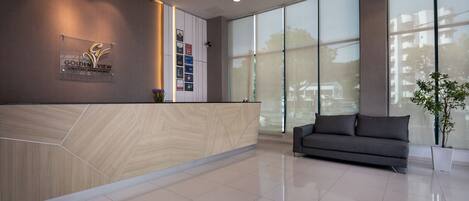 A modern reception area with a wooden reception desk, a grey sofa, and large windows offering a view of the outside.