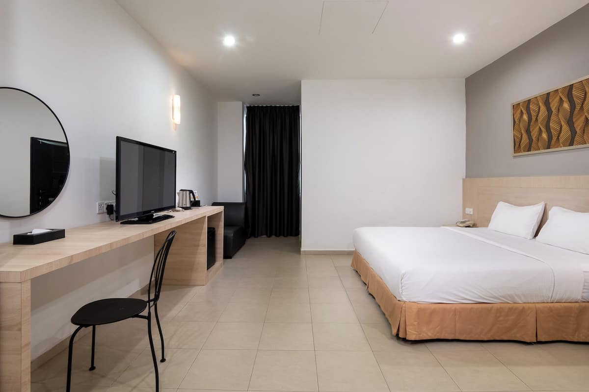 A hotel room with a bed, a desk with a computer, a chair, a TV, and a mirror.