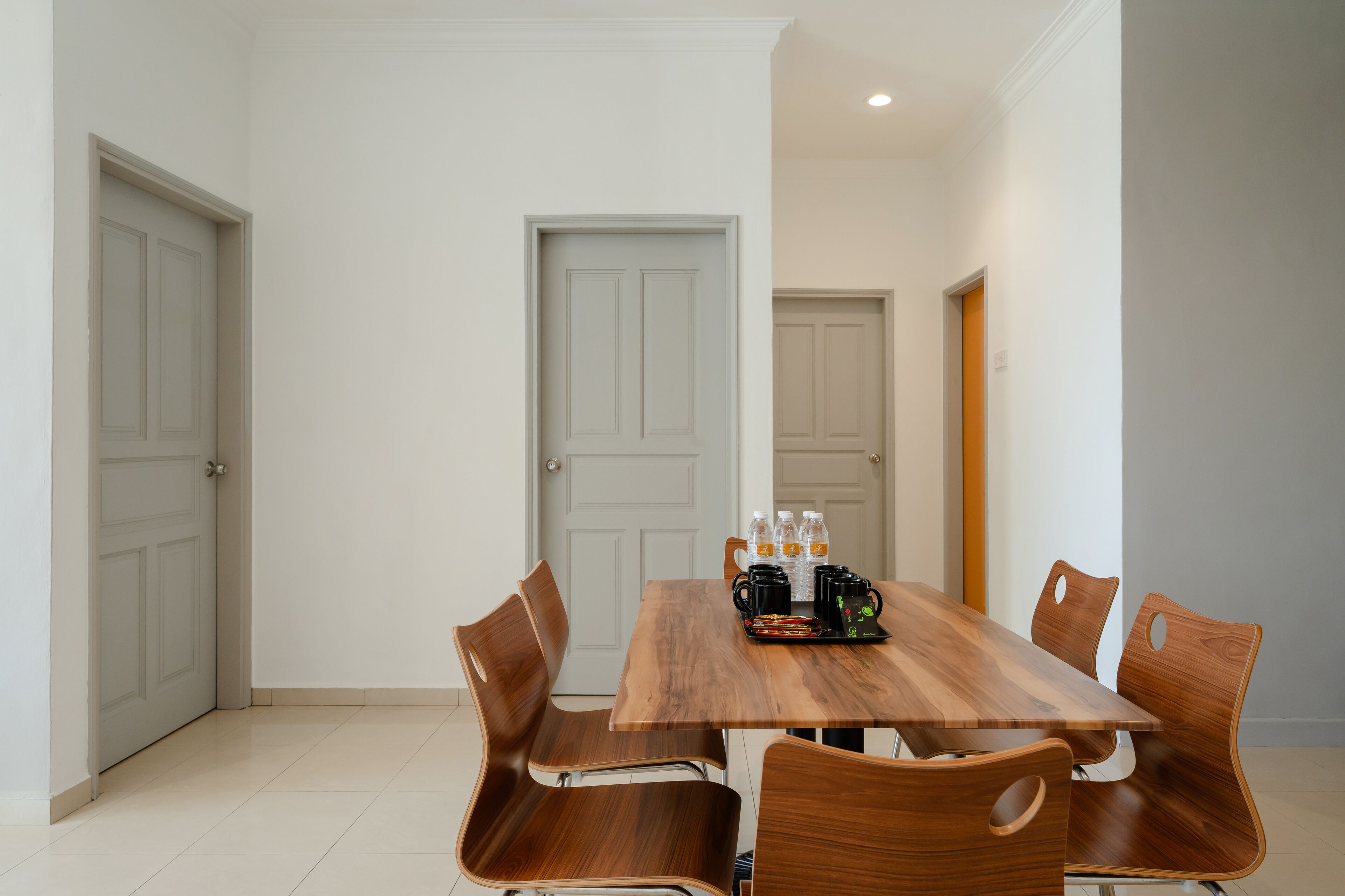 A dining area with a wooden table and matching chairs, equipped with a coffee maker, water bottles, and a tray.