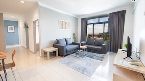 A modern living room with a grey sofa, a small table, and a desk with a computer. - Golden View Serviced Apartment (George Town)
