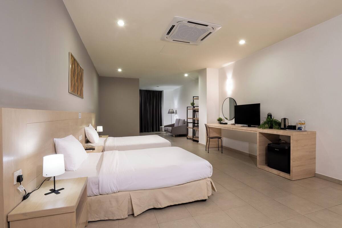 A hotel room with two beds, a desk, a TV, and a bookshelf.