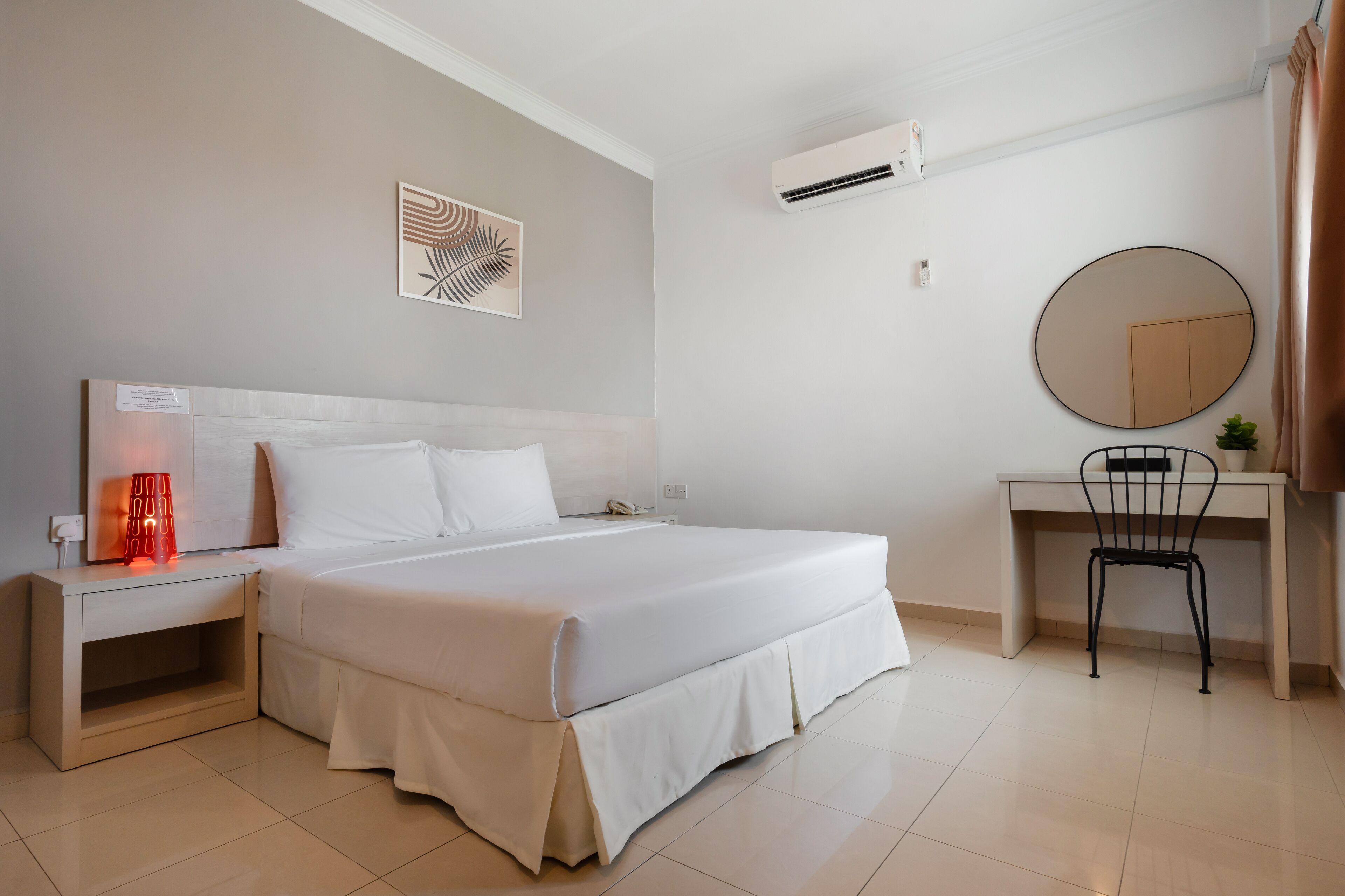 A modern hotel room with a large bed, a desk with a chair, a small plant, and a wall-mounted mirror.