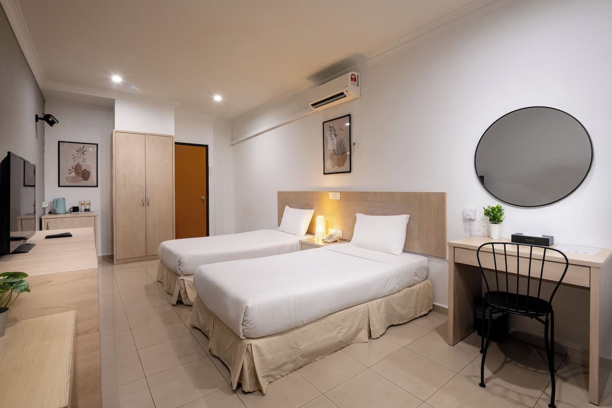 A hotel room with two beds, a desk, a chair, a TV, and a large mirror.